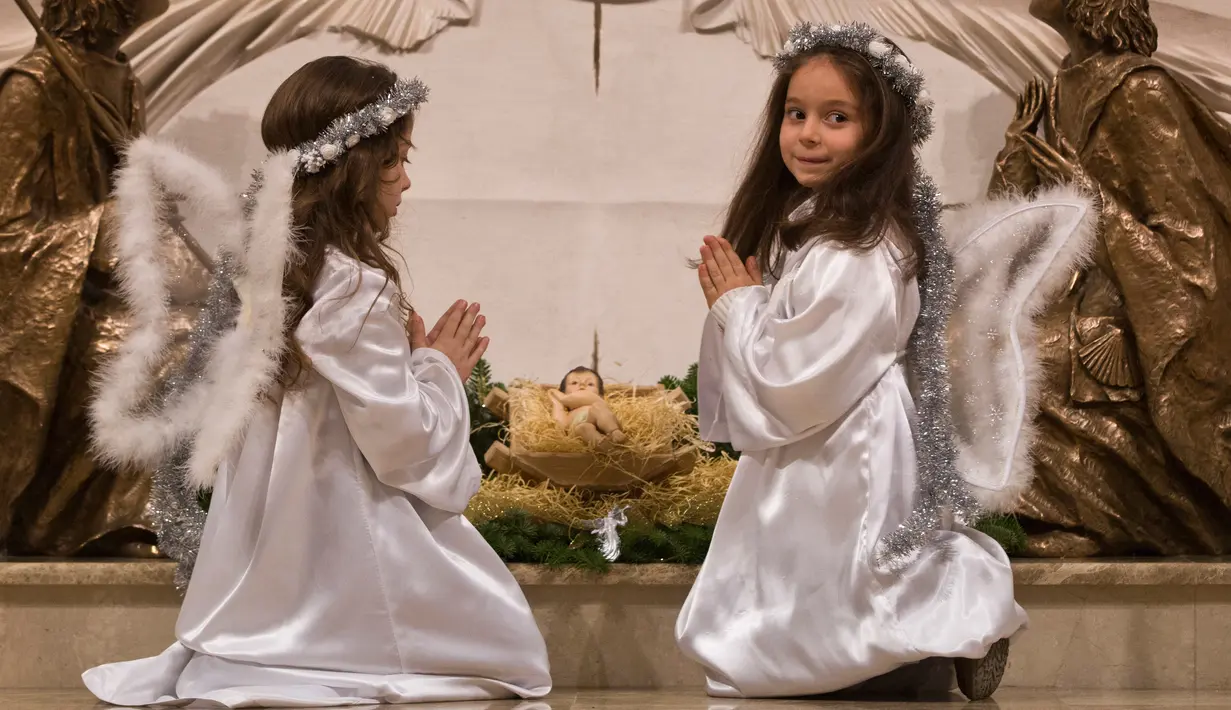 Anak-anak berpakaian seperti malaikat berdoa di depan altar pada tengah malam Natal di Katedral St. Ibu Teresa di ibukota Kosovo, Pristina (24/12). (AP Photo / Visar Kryeziu)