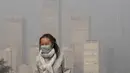 Seorang wanita mengenakan masker untuk melindungi diri dari COVID-19 berjalan di depan gedung perkantoran di Kawasan Pusat Bisnis yang diselimuti kabut polusi di Beijing, Kamis (18/11/2021).  (AP Photo/Andy Wong)