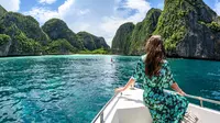 Foto diambil pada 4 Oktober 2019, seorang turis berpose di atas perahu di depan garis batas yang ditetapkan oleh Departemen Taman Nasional, Margasatwa dan Konservasi Tumbuhan Thailand untuk menutup pantai di Maya Bay bagi pengunjung di pulau selatan Thailand, Koh Phi Phi. (MLADEN ANTONOV / AFP)