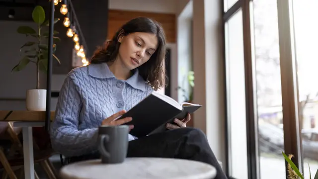 Seorang perempuan sedang membaca buku di sebuah kafe (Foto Dok: Freepik/freepik)