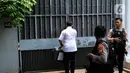 Penyidik kepolisian dengan membawa koper berwarna abu-abu gelap memasuki rumah dengan pagar dihiasi tumbuhan menjalar itu. (Liputan6.com/Herman Zakharia)
