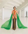 Menyanyikan lagu Kebaya bersama 5 Wanita, Andien Aisyah kenakan kebaya Janggan bermotif bunga warna oranye. Dipadukan dengan kain Batik cokelat dan selendang berwarna hijau. Rambutnya pun ditata bergaya sanggul tekuk dengan tusuk konde di bagian samping. [@andienaisyah].