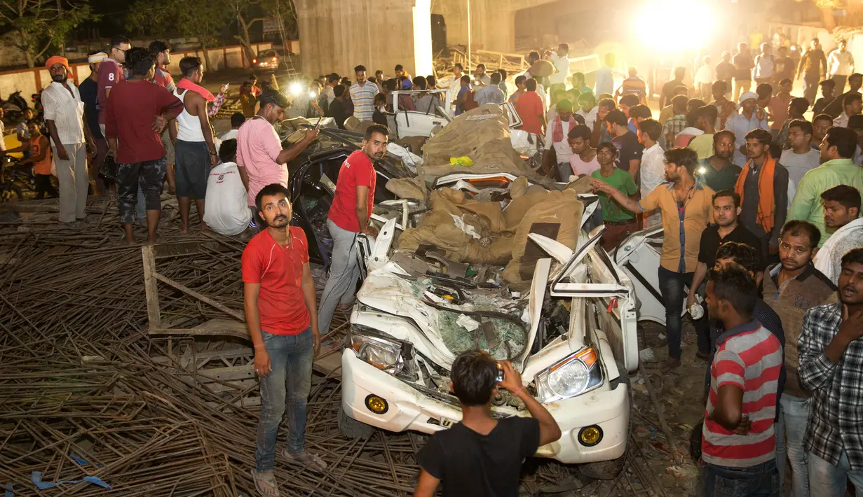 Warga India melihat sebuah mobil yang hancur tertimpa material jalan layang yang runtuh di Varanasi, Selasa (15/5). Jembatan layang itu masih dibangun ketika sebagian struktur semennya jatuh ke jalan di bawahnya. (AP/Rajesh Kumar Singh)