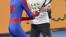Seorang aktor berpakaian seperti karakter Spider-Man meminjam raket petenis Swiss Roger Federer selama Hari Anak-anak menjelang turnamen tenis Australia Terbuka di Melbourne (13/1). (AFP Photo/Paul Crock)