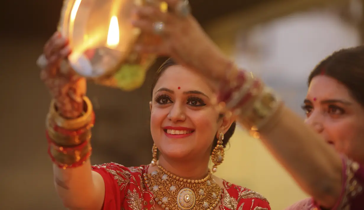 Wanita Hindu mencoba melihat bulan melalui saringan sebagai bagian dari ritual sebelum berbuka puasa sepanjang hari untuk kesejahteraan, kemakmuran, dan umur panjang suami mereka selama festival 'Karwa Chauth', di Jammu, India, Rabu (4/11/2020). (AP Photo/Channi Anand)
