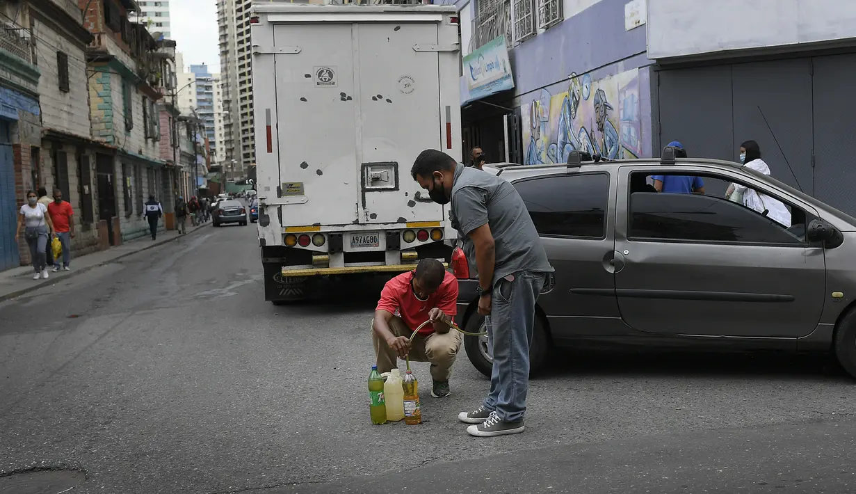 Para pria menyedot bensin mobil yang akan mereka simpan dan kemudian kembali ke pompa bensin untuk diisi lagi, di lingkungan San Juan di Caracas (19/1/2021). SPBU hanya akan mengisi tangki mobil dan motor, tetapi tidak untuk wadah agar orang tidak menyimpan bensin. (AP Photo/Matias Delacroix)