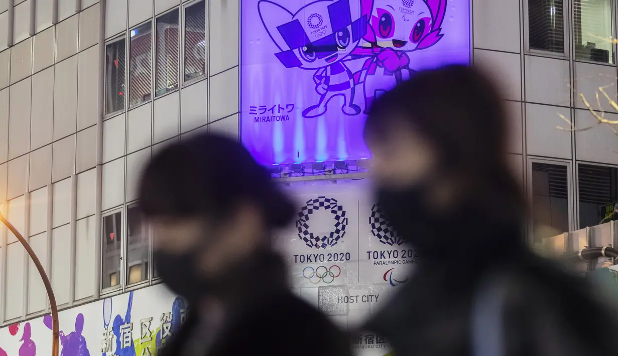 Orang-orang yang memakai masker melewati spanduk promosi Olimpiade Tokyo 2020 yang dijadwalkan ulang untuk musim panas ini, di Tokyo, Jepang, Jumat (28/1/2021). Olimpiade Tokyo digelar sesuai jadwal pada 23 Juli-8 Agustus 2021 setelah ditunda setahun karena corona Covid-19. (AP Photo/Hiro Komae)