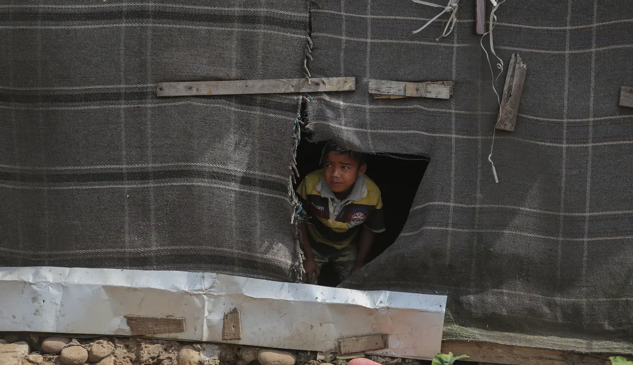 Bocah pengungsi Rohingya melihat dari selimut robek yang digunakan sebagai dinding di kamp darurat di pinggiran Jammu, 7 Maret 2021. Kepolisian India menahan lebih dari 150 pengungsi Rohingya yang kedapatan tinggal secara ilegal di wilayah Jammu dan Kashmir untuk dideportasi. (AP Photo/Channi Anand)