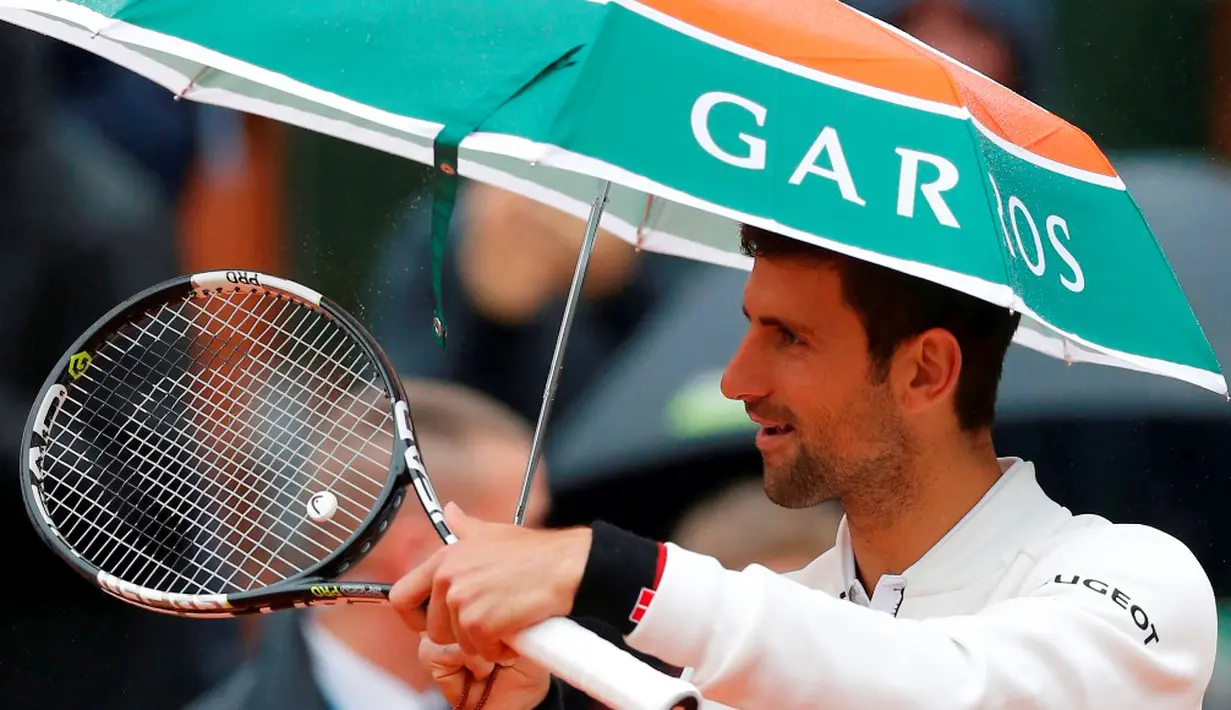 Petenis Serbia, Novak Djokovic, memakai payung saat memasuki lapangan jelang melawan petenis Spanyol, Roberto Bautista Agut, dalam laga Prancis Terbuka 2016 di Roland Garros, Prancis, (31/5/2016). (Reuters/Gonzalo Fuentes)