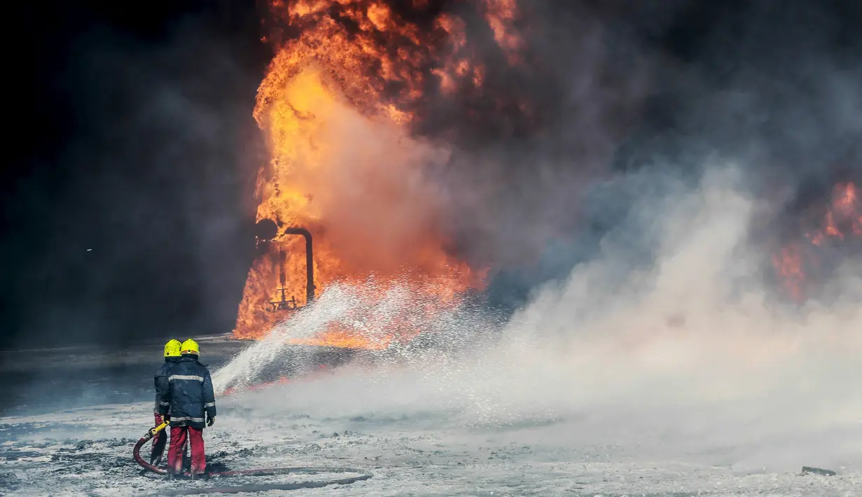 Petugas pemadam kebakaran menyemprotkan air untuk memadamkan tangki minyak yang terbakar di pelabuhan Es Sider, Libya, (6.1).  Kerusuhan yang terjadi di Libya membuat tangki minyak ini ditutup hampir lebih dari satu7 tahun. (REUTERS / Stringer)