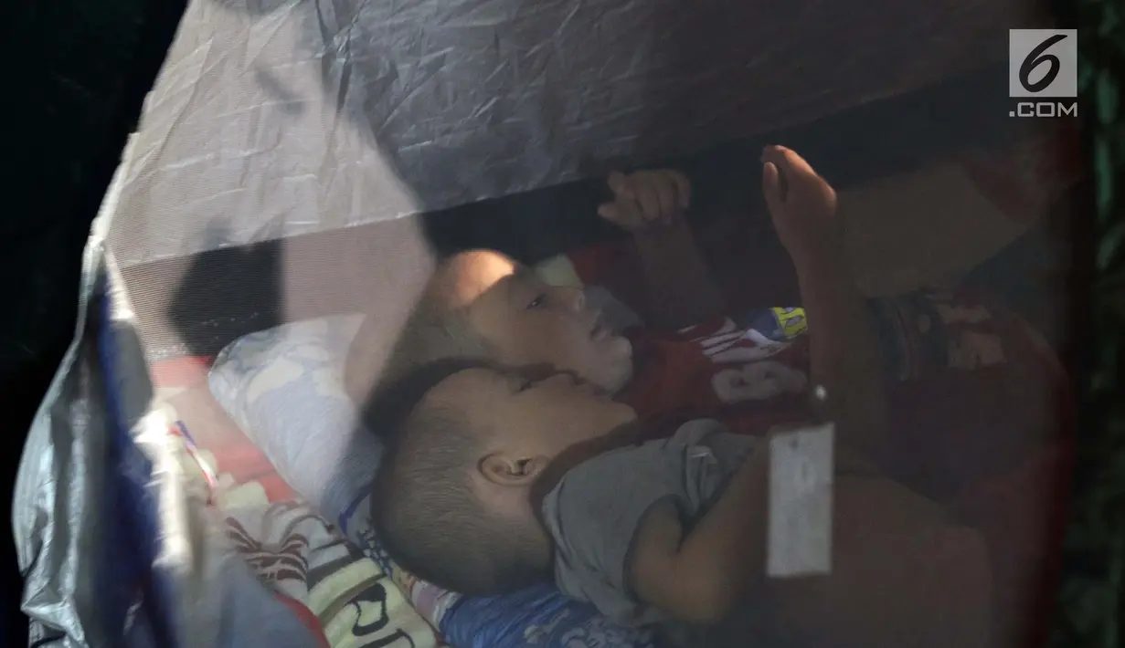 Dua anak pencari suaka bermain ponsel di dalam tenda yang dibangun di atas trotoar depan Masjid Ar-Rayan, Jalan Kebon Sirih, Jakarta, Jumat (5/7/2019). Para pencari suaka dari sejumlah negara berkonflik berharap UNHCR bisa segera memberikan jaminan perlindungan bagi mereka. (Liputan6.com/Helmi Fithr
