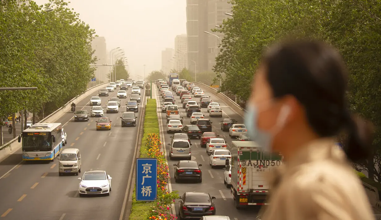 Seorang wanita yang memakai masker wajah berjalan melintasi jembatan penyeberangan saat badai pasir di Beijing, China, Kamis (6/5/2021). Debu dan badai pasir akhir musim semi mengirim indeks kualitas udara melonjak di Ibu Kota China pada hari ini. (AP Photo/Mark Schiefelbein)