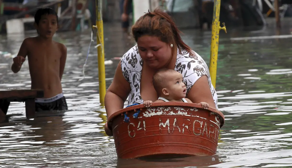 Seorang ibu membawa anaknya menyeberangi banjir di Kota Longos, Malabon City, Manila Utara, Filipina (6/7/2015). Akibat badai aktivitas penerbangan, pelabuhan dan sekolah-sekolah ditutup. (REUTERS/Romeo Ranoco)