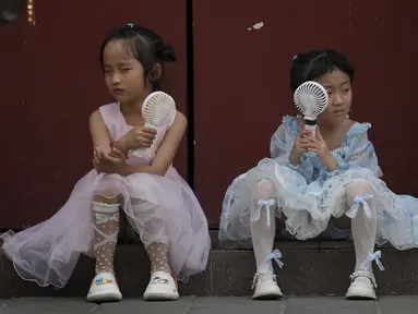 Anak-anak mendinginkan diri dengan kipas angin listrik saat beristirahat dekat Kota Terlarang pada hari yang panas di Beijing, China, 25 Juni 2023. Beijing meningkatkan level peringatan cuaca panas menjadi level tertinggi, yaitu kode merah. (AP Photo/Andy Wong)