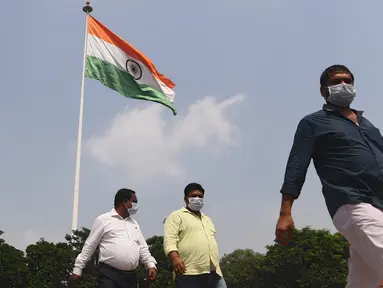 Sejumlah pria mengenakan masker berjalan melewati bendera nasional India di New Delhi (16/9/2020). Total kasus Covid-19 di India melampaui lima juta pada 16 September, data kementerian kesehatan menunjukkan Pandemi meluas cengkeramannya di negara tersebut. (AFP/Sajjad Hussan)