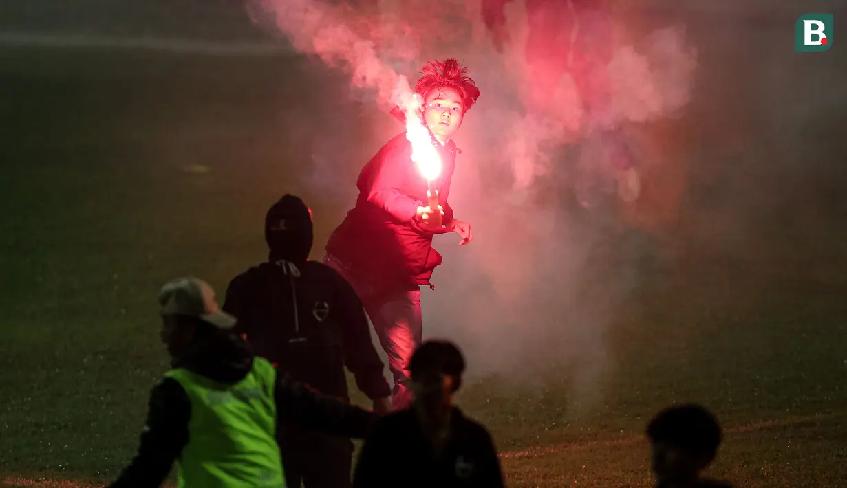 <p>Seorang suporter menyalakan flare di dalam lapangan saat berlangsungnya laga leg kedua final Pegadaian Liga 2 2023/2024 antara Semen Padang mengadapi PSBS Biak di Stadion GOR Haji Agus Salim, Padang, Sabtu (9/3/2024). (Bola.com/Bagaskara Lazuardi)</p>
