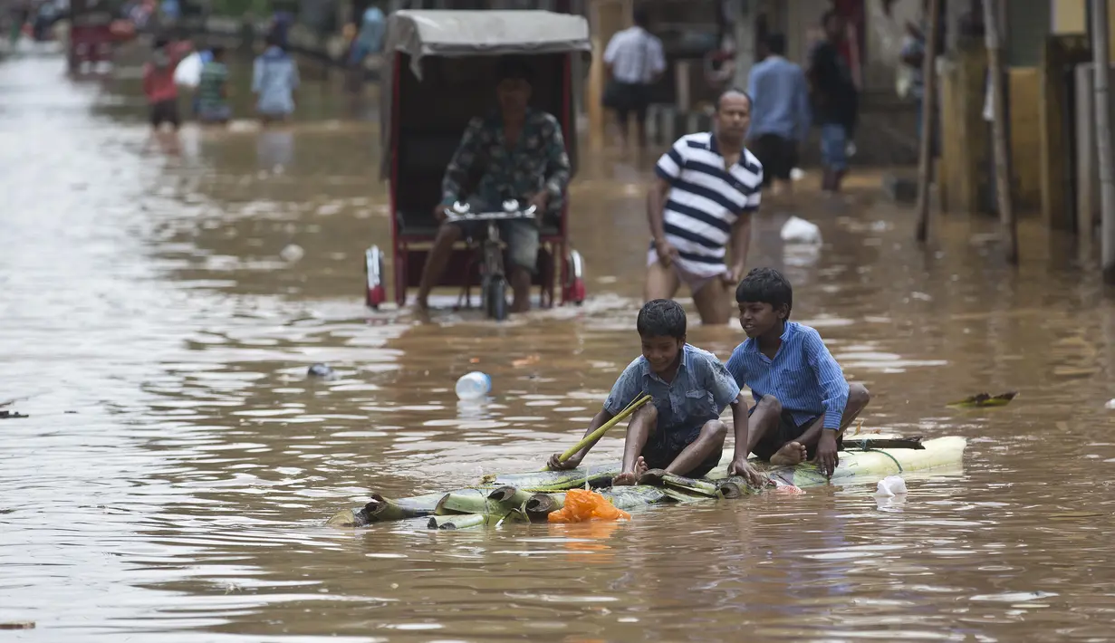 Dua orang anak bermain saat banjir melanda kawasan mereka di Gauhati, India, Rabu (14/6). Angin monsun yang mendatangi India berdampak pada tingginya curah hujan yang menyebabkan banjir. (AP Photo / Anupam Nath)