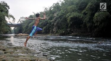 Seorang anak melompat ke Sungai Ciliwung, Depok, Jawa Barat, Kamis (4/7/2019). Menurunnya debit air Sungai Ciliwung akibat musim kemarau dimanfaatkan warga setempat sebagai tempat wisata gratis untuk mengajak anak berenang. (merdeka.com/Iqbal Nugroho)
