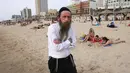 Seorang pria Yahudi Ultra-Ortodoks berjalan di pantai di kota pesisir Israel Tel Aviv (19/4/2021). Pemerintah Israel mencabut kewajiban memakai masker setelah 81 persen penduduk dewasa menerima vaksin Covid-19. (AFP/menahem kahana)