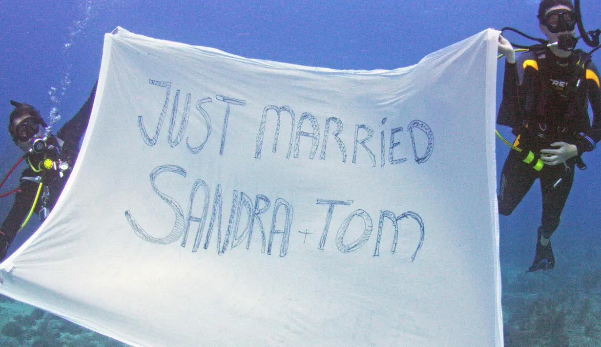Sahabat Sersan Thomas Mould dan Sandra Hyde menujukkan kain bertuliskan Just Married saat prosesi pernikahan di Florida Keys National Marine Sanctuary (21/12). Pasangan ini bertemu di Keys pada tahun 2013. (Frazier Nivens/Florida Keys News Bureau via AP)