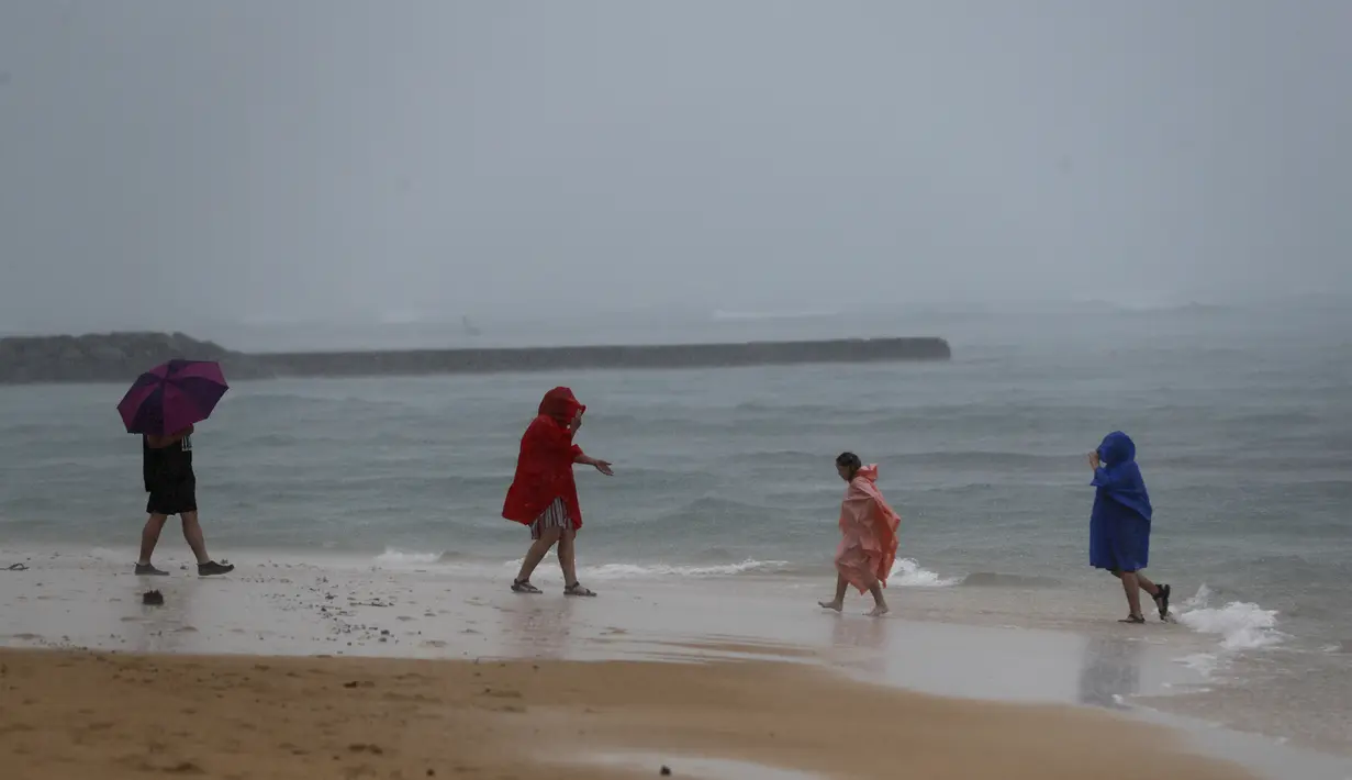 Pengunjung pantai bermain hujan di Pantai Waikiki, Honolulu  (6/12/2021). Badai kuat yang membawa angin kencang dan hujan yang sangat deras membanjiri jalan-jalan dan meruntuhkan kabel listrik dan cabang-cabang pohon di seluruh Hawaii. (AP Photo/Marco Garcia)