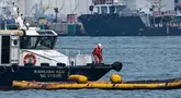 Seorang pekerja pembersihan di atas kapal berdiri di atas alat penyedot minyak selama operasi untuk membersihkan minyak dari tumpahan minyak di dekat terminal pelabuhan Pasir Panjang di Singapura pada tanggal 18 Juni 2024. (ROSLAN RAHMAN/AFP)