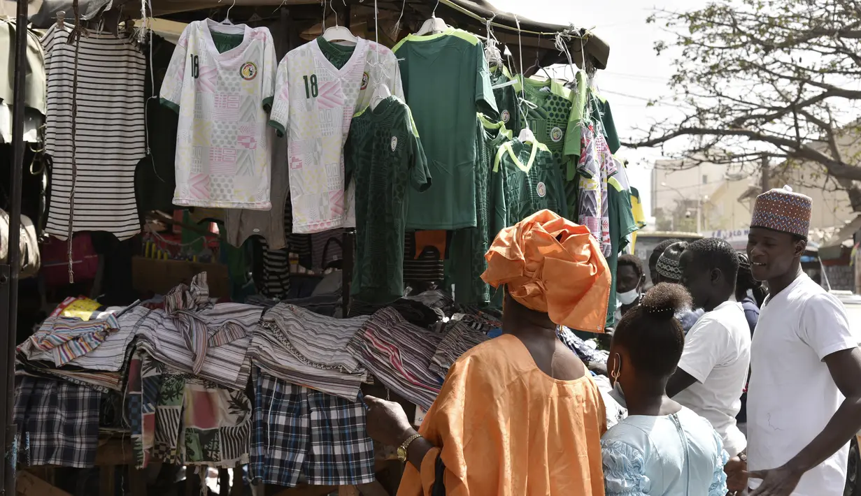Warga melihat Jersey tim nasional Senegal yang dipajang untuk dijual di jalan-jalan Dakar (4/2/2022). Senegal akan bertanding melawan Mesir pada babak final Piala Afrika 2021 di Paul Biya stadium, Senin (7/2/2022) dini hari WIB besok. (AFP/Seyllou)