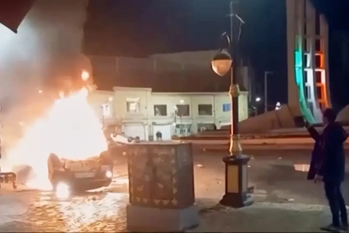 Cuplikan gambar dari video yang dirilis pada Jumat (9/1/2026) oleh televisi pemerintah Iran memperlihatkan seorang pria memegang sebuah perangkat untuk mendokumentasikan kendaraan yang terbakar selama aksi protes massal pada malam hari di Zanjan, Iran.