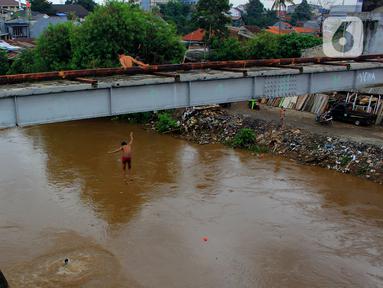 Seorang anak nekat melompat dari jembatan ke Kali Ciliwung Kalibata, Jakarta, Selasa (25/2/2020). Kali Ciliwung meluap usai hujan deras mengguyur Jakarta dan sekitarnya pada kemarin malam. (merdeka.com/magang/Muhammad Fayyadh)