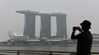 Seorang pria mengambil gambar ketika Hotel dan Resor Marina Bay Sands diselimuti kabut asap, Singapura, Rabu (18/9/2019). Badan Meteorologi Klimatologi dan Geofisika (BMKG) mendeteksi sebaran asap akibat kebakaran hutan dan lahan di Sumatra mencapai Singapura dan Malaysia. (Roslan RAHMAN/AFP)