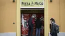 Orang-orang mengantre di mesin penjual pizza otomatis, yang pertama dari jenisnya di pusat kota Roma, Italia pada 29 April 2021. Mesin penjual otomatis ini mampu menguleni adonan, membumbui, memasak, dan menyajikan pizza dalam kotak karton hanya dalam waktu tiga menit. (Filippo MONTEFORTE/AFP)