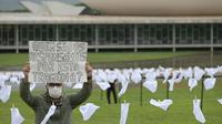 Seorang aktivis dari kelompok hak asasi manusia Rio de Paz memegang poster bertuliskan 'Siapa yang bertanggung jawab atas tragedi ini?' di antara sapu tangan putih yang mewakili warga Brasil yang meninggal karena COVID-19 di depan Kongres Nasional di Brasilia, Senin (18/10/2021). (EVARISTO SA / AFP)