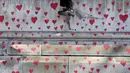 Seorang perempuan makan sambil duduk di atas Tembok Peringatan COVID-19, dengan lukisan hati di seberang Gedung Parlemen, di London, Senin (29/3/2021). Mural hampir 150.000 lukisan hati itu untuk mengenang ribuan orang yang meninggal akibat virus corona di Inggris. (Lucianna Guerra/PA melalui AP)