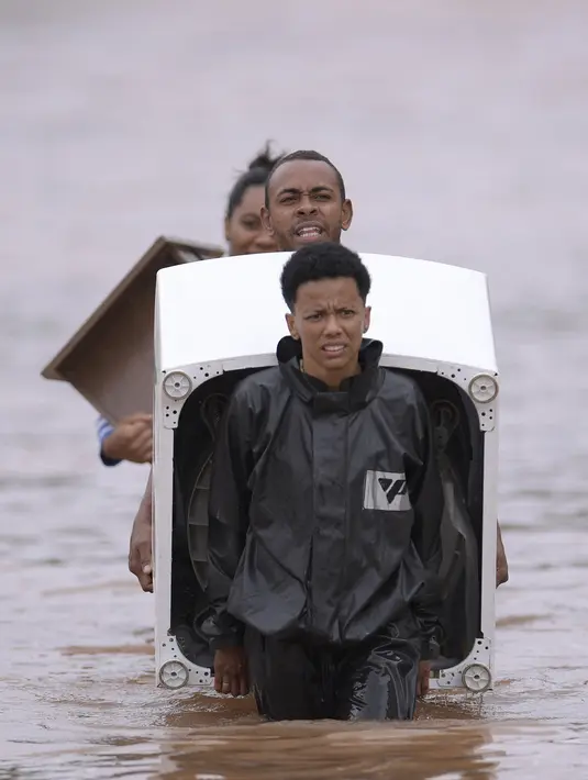 Orang-orang mengarungi air saat mereka memindahkan barang-barang dari rumah mereka yang terendam banjir di negara bagian Minas Gerais di kotamadya Juatuba, Brasil (10/1/2022). Hujan deras yang turun dalam beberapa hari terakhir di bagian tenggara negara itu membuat banjir besar. (AFP/Douglas Magno)