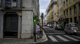 Dua orang menunggu untuk menyeberang jalan di pusat kota Lisbon, Portugal, Senin (13/9/2021). Portugal hari ini mengakhiri aturan wajib penggunaan masker di jalan-jalan. (PATRICIA DE MELO MOREIRA / AFP)