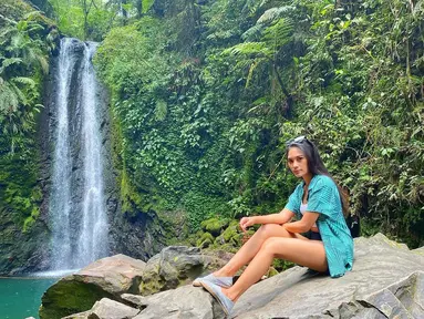 Garneta Haruni nampak santai dengan kemeja biru dan sepatu slip on. Ia nampak sedang menikmati liburannya di sebuah air terjun di daerah Jawa Barat. (Liputan6.com/IG/@garnetaharuni).