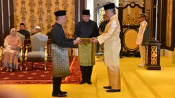 Muhyiddin Yassin (kiri) menerima dokumen dari Raja Sultan Abdullah Sultan Ahmad Shah (kanan) sebelum disumpah sebagai Perdana Menteri Malaysia di Istana Negara, Kuala Lumpur, Minggu (1/3/2020). Muhyiddin Yassin menggantikan Mahathir Mohamad. (MASZUANDI ADNAN/MALAYSIA'S DEPARTMENT OF INFORMATION/AFP)
