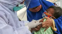 Bidan lengkap dengan baju Alat Pelindung Diri (APD) memberi imunisasi pada anak di Posko Imunisasi, Kelurahan Bakti Jaya, Tangerang Selatan, Senin (11/5/2020). Imunisasi sesuai jadwal akan membantu sistem imun anak memproduksi antibodi saat pandemi Covid-19. (Liputan6.com/Fery Pradolo)