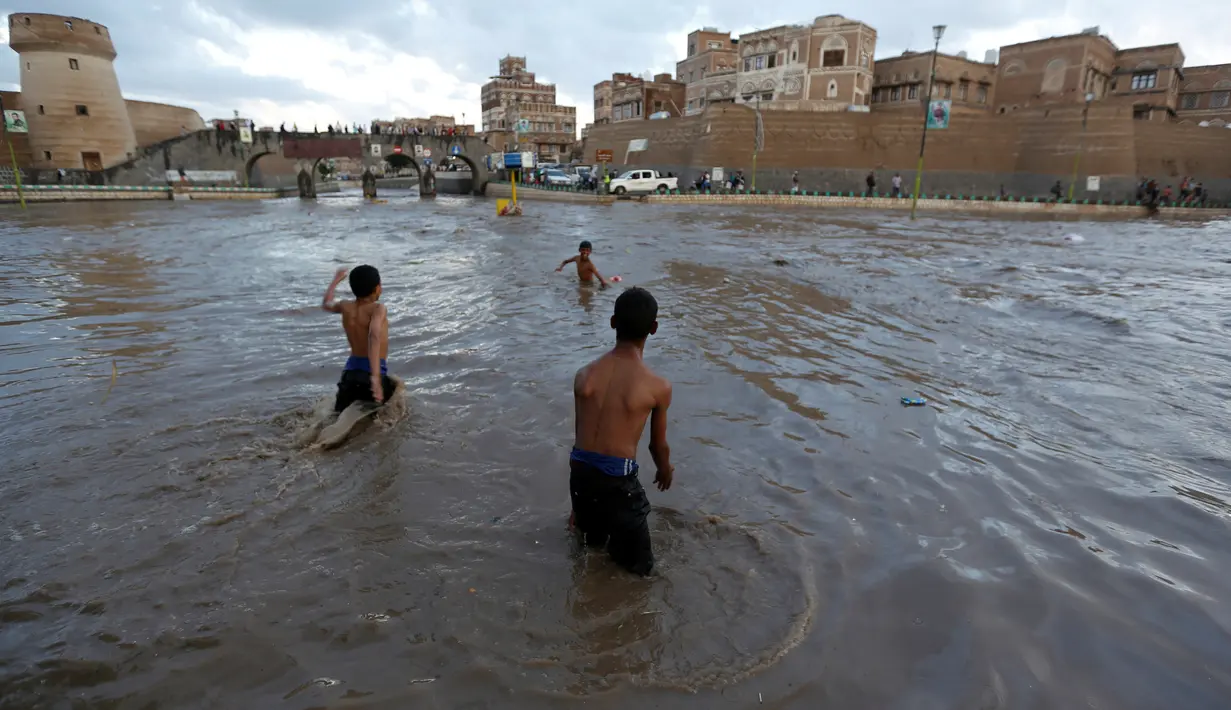 Sejumlah anak bermain di tengah banjir di Sanaa, Yaman, Selasa (2/8). Hujan lebat yang mengguyur Sanaa membuat salah satu ruas jalan di kota itu berubah seakan menjadi sungai. (REUTERS / Khaled Abdullah)