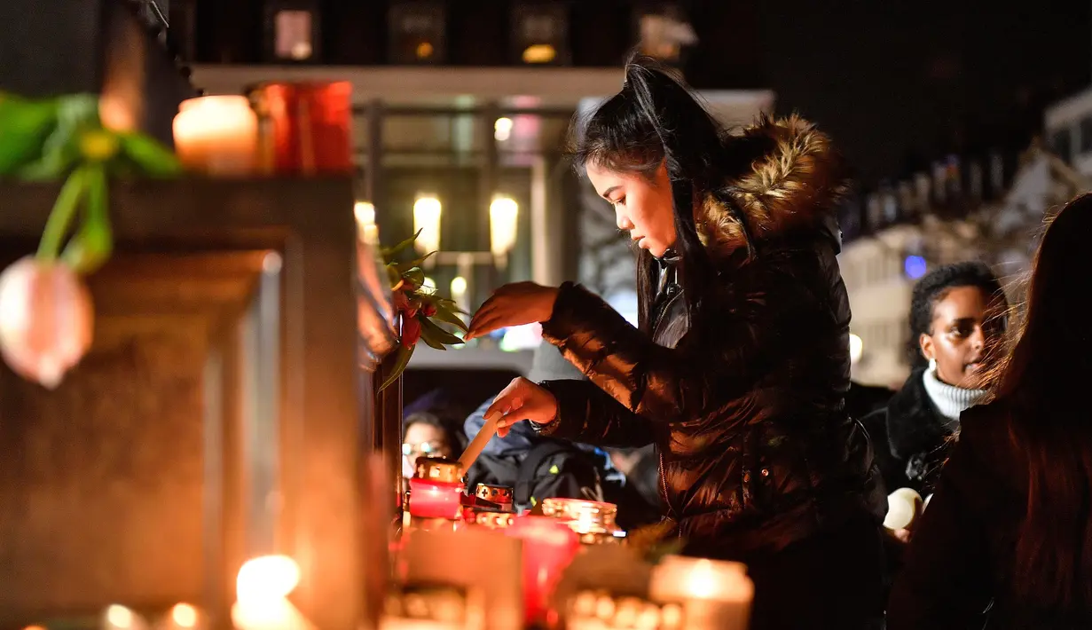 Seorang wanita menyalakan lilin saat berkabung untuk para korban penembakan brutal di Hanau, Jerman, Kamis (20/2/2020). Semua korban penembakan memiliki latar belakang imigran. (AP Photo/Martin Meissner)