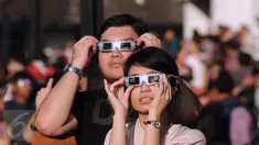 Sepasang muda mudi menggunakan kacamata khusus untuk melihat proses gerhana matahari di sekitar Taman Ismail Marzuki, Jakarta, Rabu (9/3/2016). Di Jakarta, fenomena gerhana matahari 90% bisa diamati selama 2,11 menit. (Liputan6.com/Helmi Fithriansyah)   