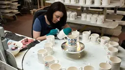 Pekerja melukis dengan tangan sebuah mug untuk merayakan pernikahan Pangeran Harry dan Meghan Markle di pabrik Emma Bridgewater di Stoke-on-Trent, Inggris (16/4). (AFP/Oli Scarff)