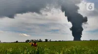 Petani beraktivitas dengan latar belakang akibat kebakaran Kilang Balongan di Indramayu, Jawa Barat, Senin (29/03/2021). Kilang Balongan milik PT Pertamina di Indramayu terbakar pada 29 Maret 2021 mulai sekitar pukul 00.45 dini hari. (merdeka.com/Arie Basuki)