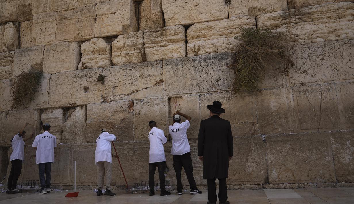 Para pekerja memindahkan catatan doa yang ditinggalkan pengunjung dari celah di antara batu-batu di Tembok Barat, situs paling suci tempat orang Yahudi dapat berdoa di Kota Tua Yerusalem, Selasa, 20 September 2022, menjelang Rosh Hashana, Tahun Baru Yahudi. Catatan dimakamkan di pemakaman terdekat menurut tradisi Yahudi. Operasi dilakukan dua kali setahun sebelum Rosh Hashana dan sebelum liburan Paskah di musim semi. (AP/Mahmoud Illean)