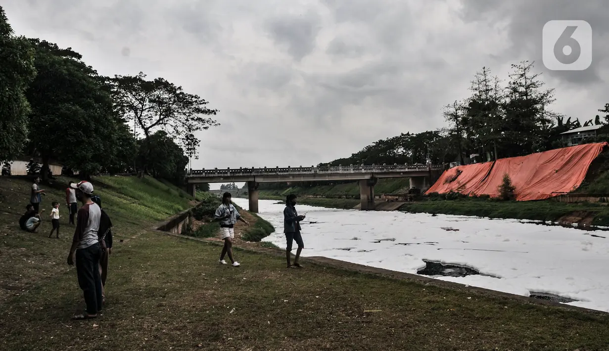 Warga bermain di pinggir aliran Kanal Banjir Timur (KBT), Duren Sawit, Jakarta, Kamis (2/7/2020). Penampakan busa yang memenuhi aliran KBT akibat limbah pabrik dan rumah tangga sejak dua minggu lalu itu menjadi tontonan warga meski menimbulkan bau tak sedap. (merdeka.com/Iqbal Nugroho)
