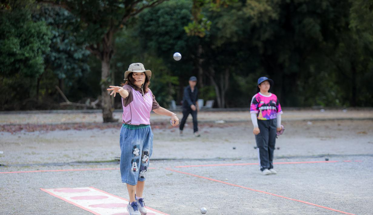 Bertempat di Lapangan Latih Dua Kompleks 700th Anniversary of Chiang Mai Stadium, pada Kamis (11/12/2025) terlihat pemain muda hingga tua saling bersaing melemparkan bola logam tersebut. Tampak dalam foto, warga saat memainkan olahraga Petanque di Lapangan Latih Dua Kompleks 700th Anniversary of Chiang Mai Stadium, Thailand, Kamis (11/12/2025). (Bola.com/Bagaskara Lazuardi)