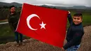 Dua pemuda membentangkan bendera sebagai dukungannya terhadap tentara Turki yang sedang memerangi milisi Kurdi di Suriah, Kilis, Turki, Jumat (26/1). (AP Photo/Lefteris Pitarakis)