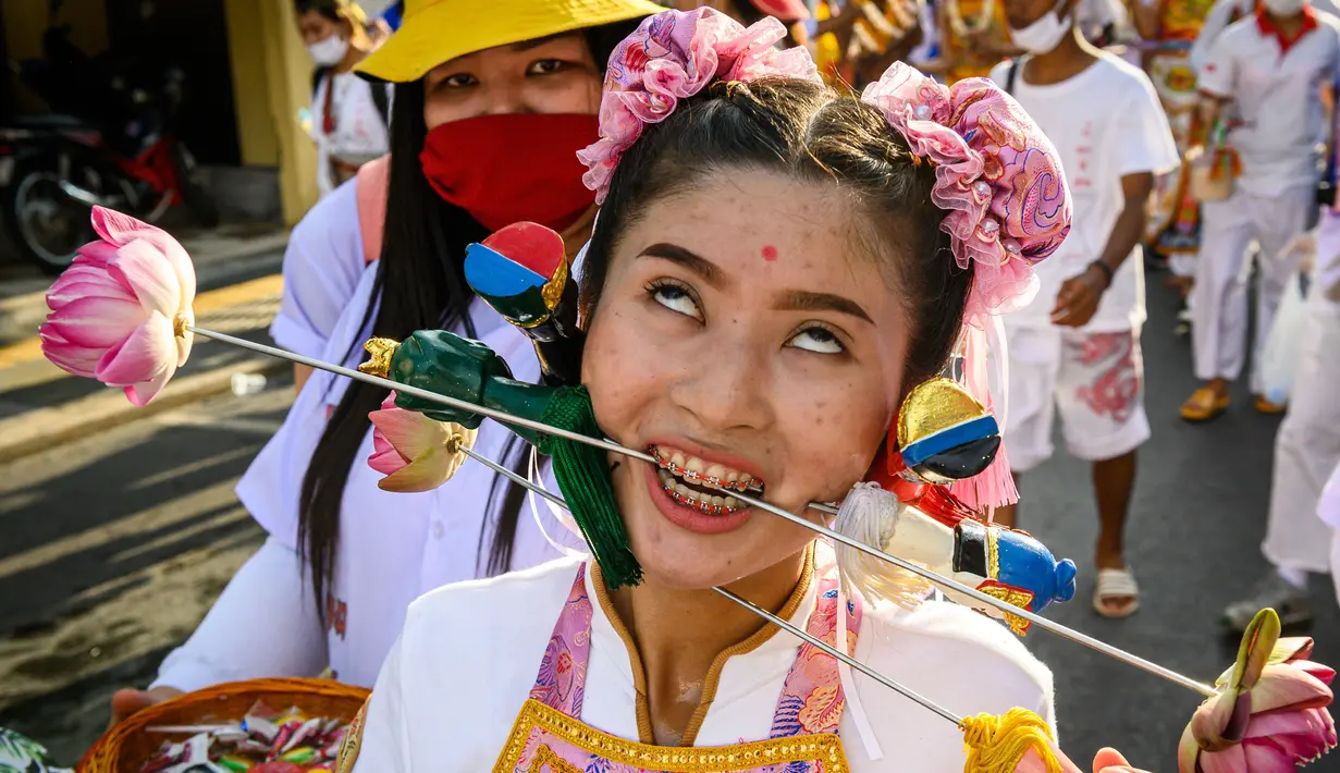 Seorang wanita menusuk pipinya dengan besi  saat mengikuti prosesi perayaan Festival Vegetarian tahunan di Phuket, Thailand, Kamis (3/10/2019). Festival ini biasanya berlangsung selama 9 hari di akhir September sampai Oktober. (AFP Photo/Mladen Antonov)