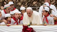 Paus Fransiskus meniup lilin kue ulang tahunnya yang tertancap di atas pizza panjang bersama dengan anak-anak di Vatikan, Minggu (17/12). Pizza dibuat berbentuk persegi panjang diratakan dari ujung ke ujung di atas meja. (L'Osservatore Romano/Pool via AP)