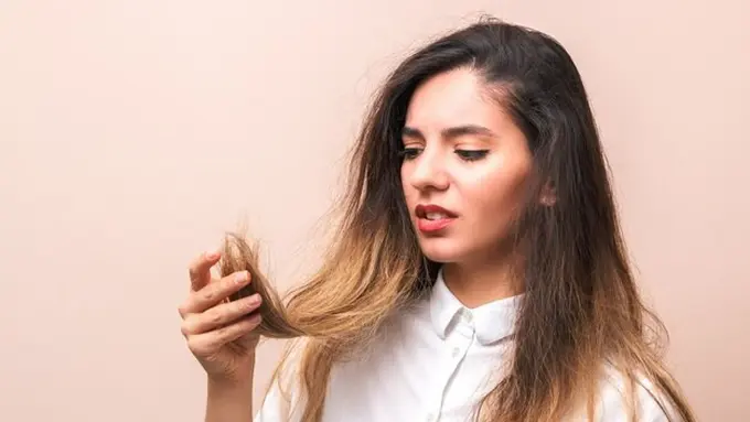 Seorang perempuan berbaju putih sedang memegang rambutnya yang tampak kering dan rusak (Foto Dok: Freepik/user15503477)
